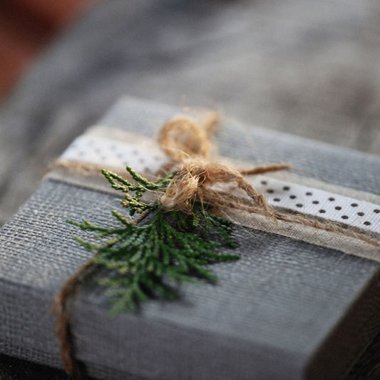 Christmas gift box wrapped in gray paper and twine, decorated with evergreen sprig on rustic wooden surface.