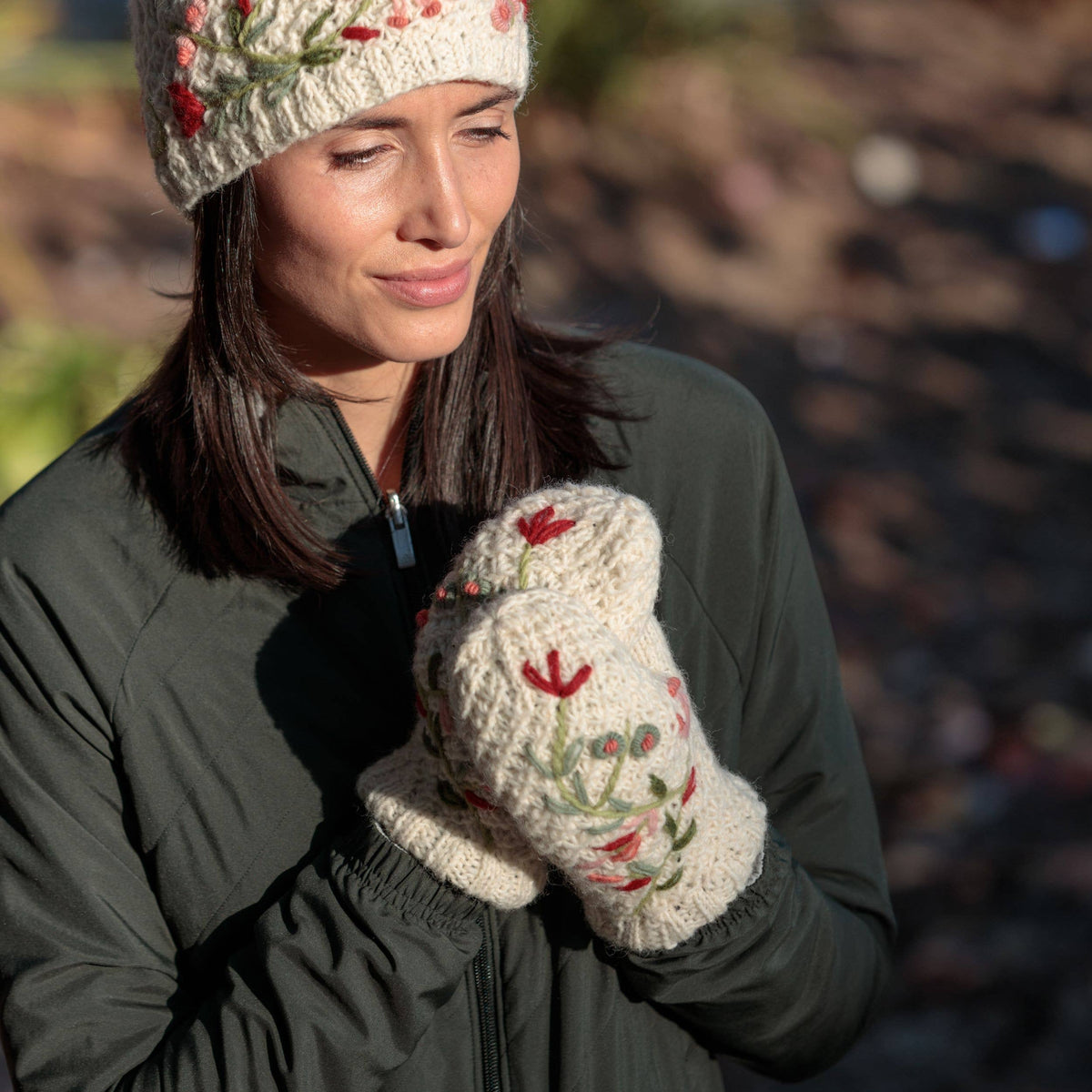 Wool hand-knit mittens in light natural with embroidered flowers, worn at chest level.